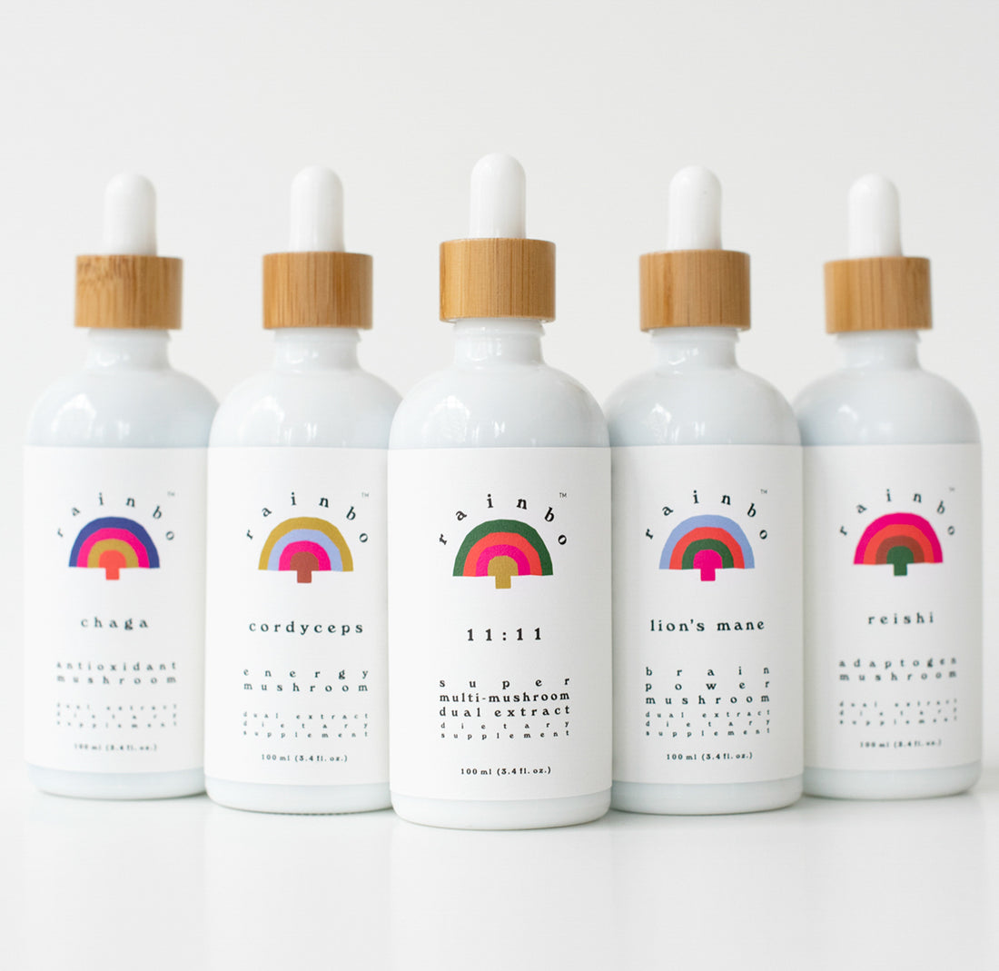 There are 5 individual tinctures in a row with a white background. Each tincture is fully white with text on it and the rainbo logo which is a rainbow. The tinctures in the photo are chaga, cordyceps, 11:11, lion's mane and reishi.