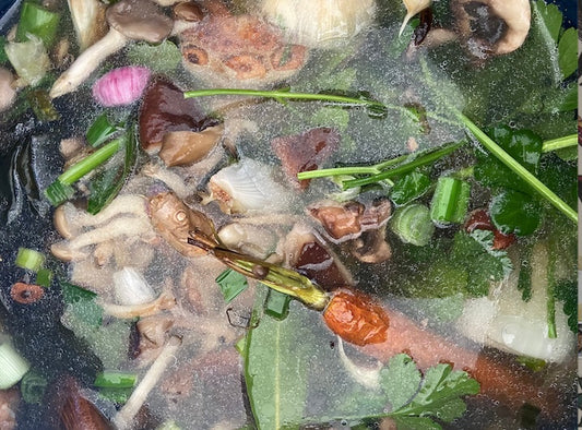 There are a bunch of green, orange and pink vegetables in water that are starting to boil into a broth