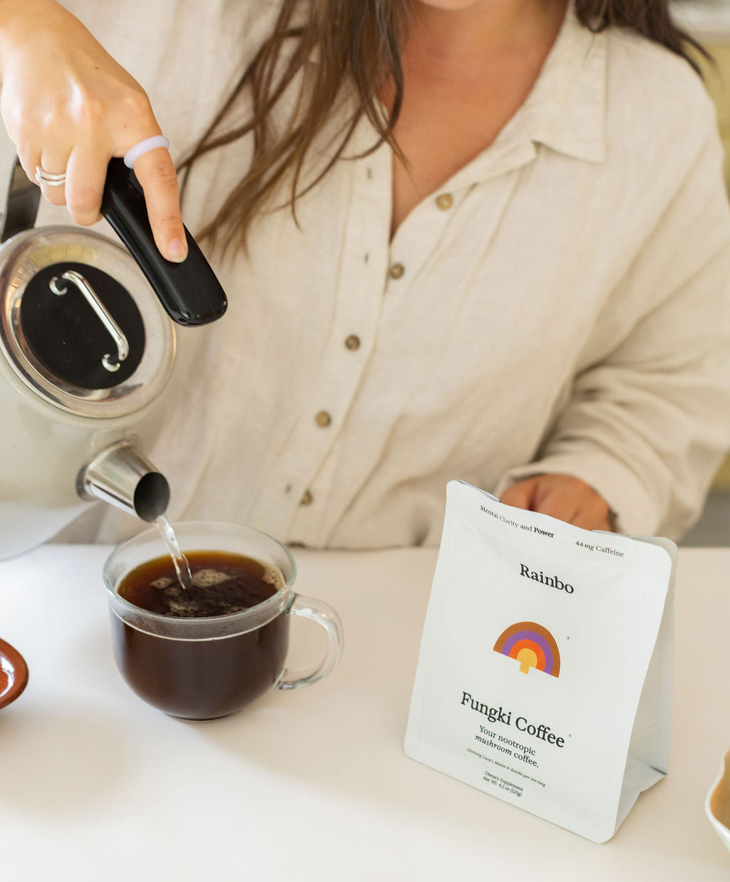 Person pouring coffee into a cup with a Rainbo Fungki Coffee package on a table.