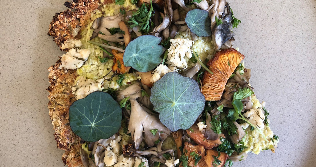 cauliflower crust pizza topped with mushrooms, nut cheese, parsley and nasturtium