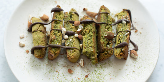 6 chewy matcha biscotti on a plate drizzled with chocolate sauce on top and sprinkled with matcha powder
