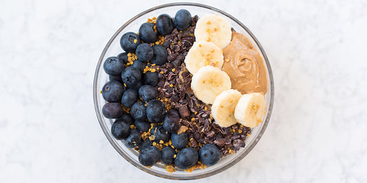 bowl of chia seed pudding topped with blueberries, cacao nibs, bee pollen, bananas and nut butter