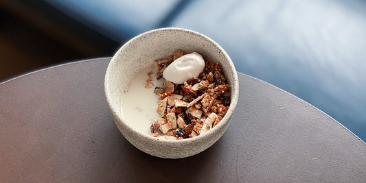 bowl of granola with nut milk and scoop of coconut yogurt. granola has goji berries, toasted coconut flakes and hemp seeds