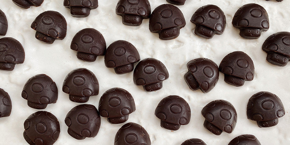 a munch of small mushroom shaped chocolates are lined up on a baking sheet with parchment paper