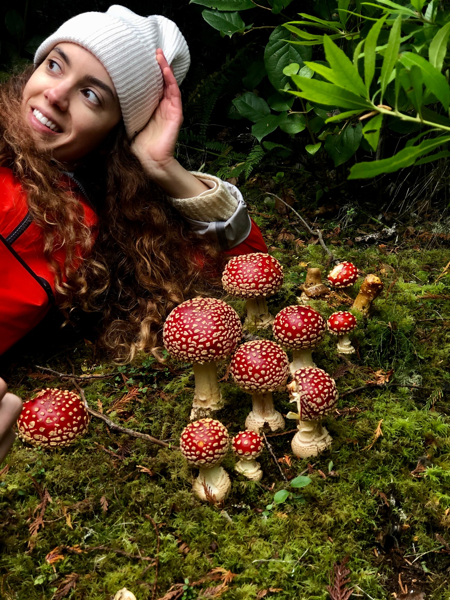 Tonya Papanikolov, founder of Rainbo laying on the grass with a community of 10 red amanita muscaria mushrooms